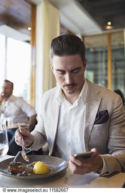 Businessman using mobile phone while sitting at restaurant eating lunch