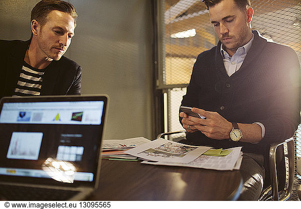Businessman using mobile phone while sitting with male colleague in office