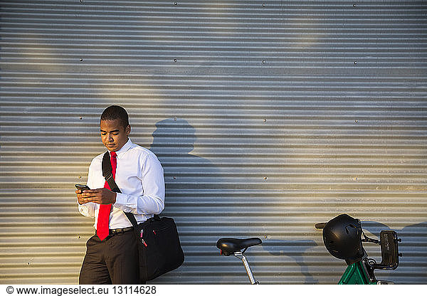 Businessman using mobile phone while standing against closed shutter