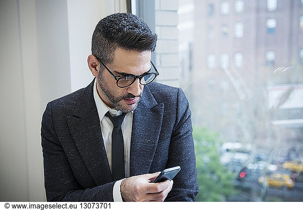 Businessman using phone by window in office