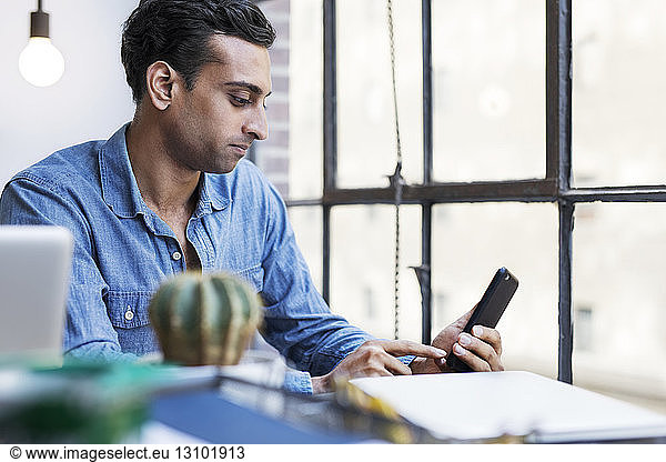 Businessman using phone while sitting at desk in office
