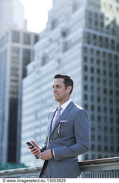 Businessman using phone while standing against buildings in city