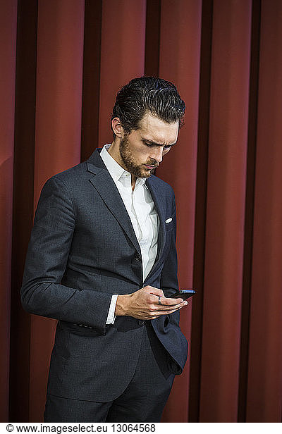 Businessman using phone while standing against maroon patterned wall
