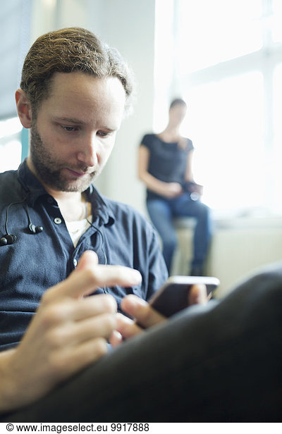 Businessman using smart phone in creative office with female colleague in background