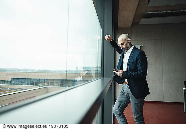 Businessman using smart phone leaning on glass window