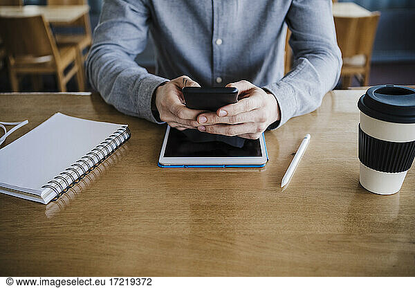 Businessman using smart phone over digital tablet on desk at work place