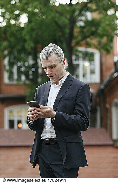 Businessman using smart phone standing on street