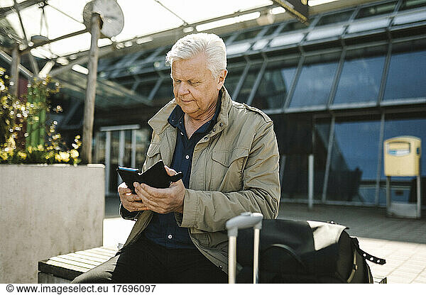 Businessman using smart phone while sitting on bench at railroad station