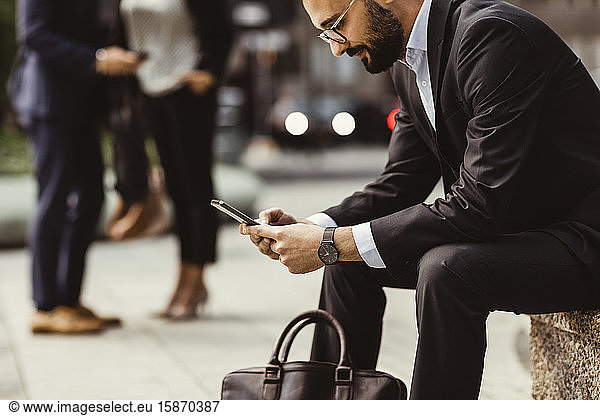 Businessman using smart phone while sitting on seat outdoors