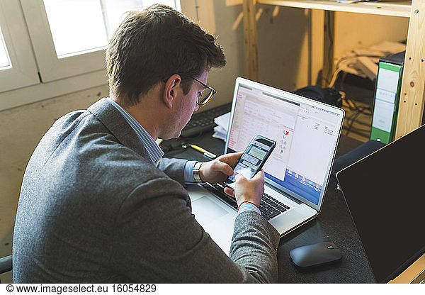 Businessman using smartphone and laptop at desk in office