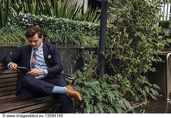 Businessman using tablet computer while sitting on sidewalk bench