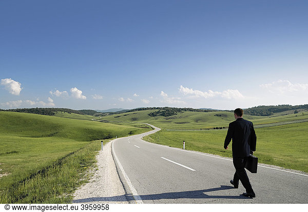 Businessman walking along a lonely country road rear view