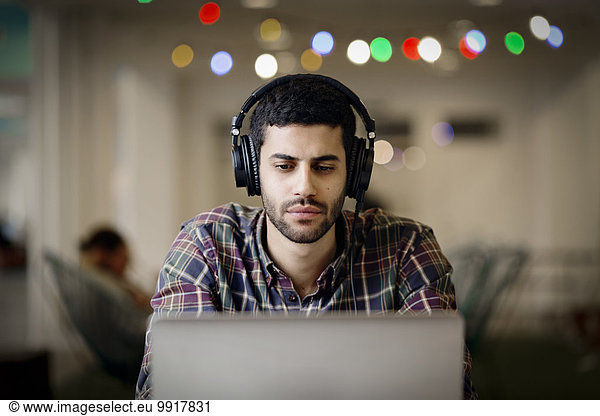 Businessman wearing headphones while working late on laptop in creative office