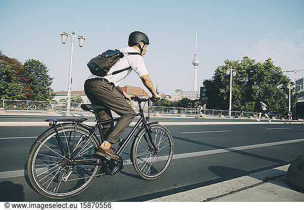 Businessman wearing helmet riding bicycle on road in city against sky