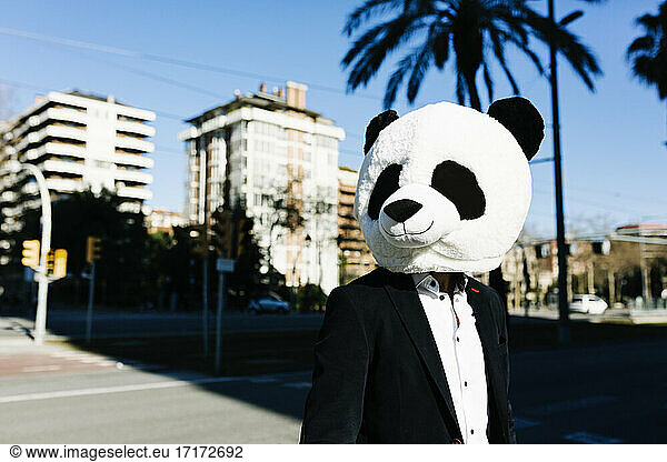 Businessman wearing panda mask looking away while standing in city