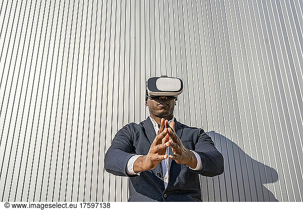 Businessman wearing virtual reality simulator standing with hands clasped in front of wall