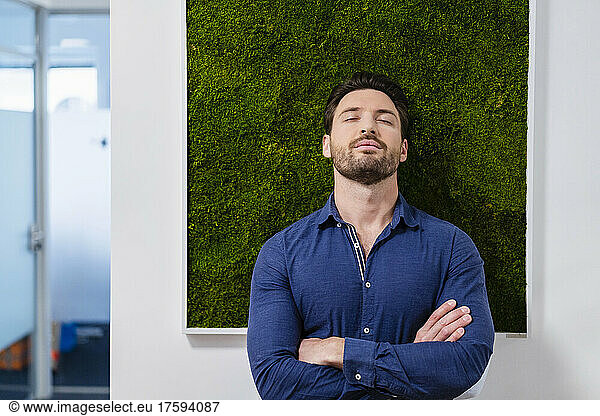Businessman with arms crossed in front of wall at office