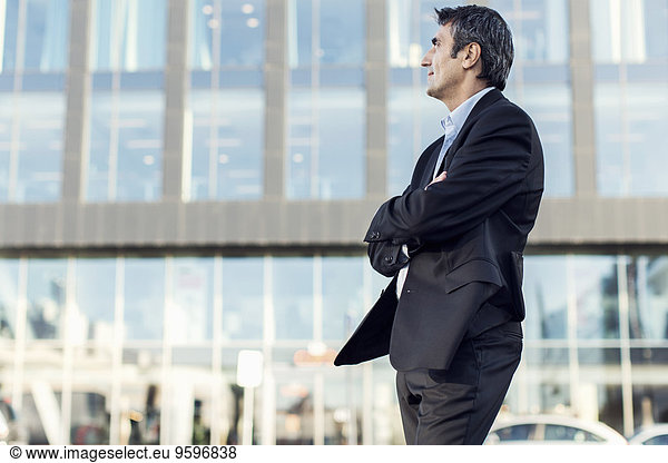Businessman with arms crossed looking away outside office building
