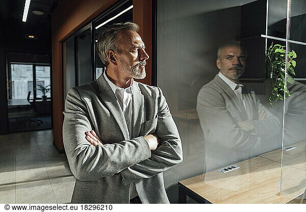 Businessman with arms crossed standing by glass
