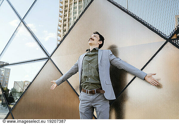 Businessman with arms outstretched in front of modern office building
