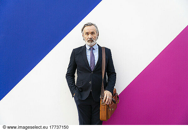 Businessman with bag standing in front of multi colored wall