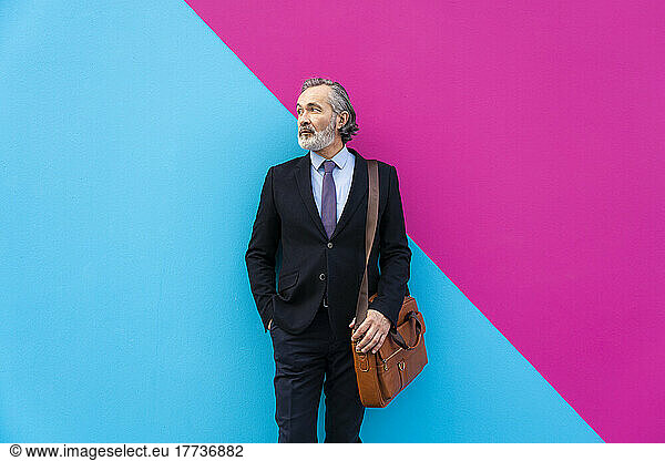 Businessman with bag standing in front of pink and blue wall