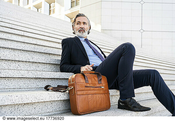 Businessman with beard sitting by bag on steps