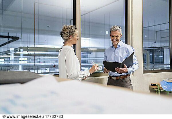 Businessman with clipboard and businesswoman with digital tablet talking in factory office