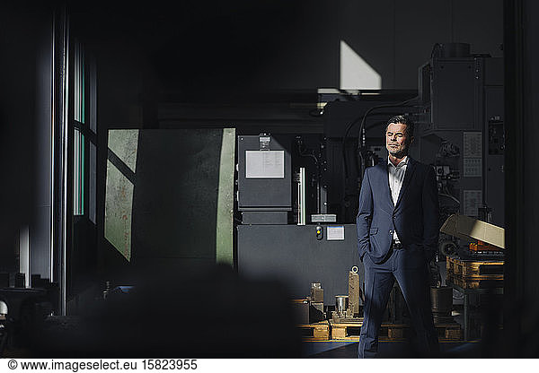 Businessman with closed eyes standing in a factory