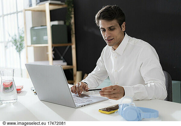 Businessman with credit card doing online shopping through laptop at office