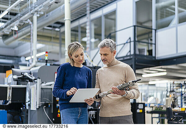 Businessman with device and businesswoman with digital tablet talking in factory