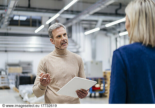 Businessman with digital tablet talking to businesswoman in factory