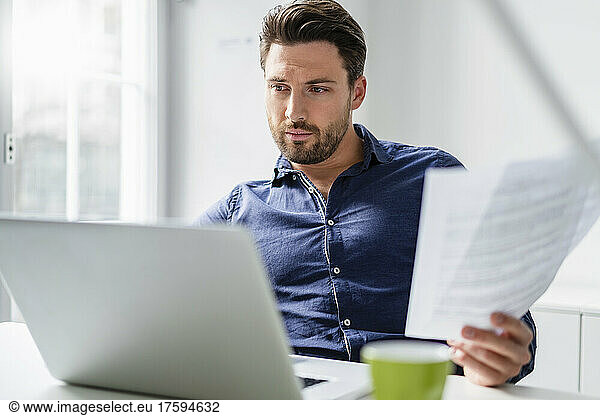 Businessman with document working on laptop in office