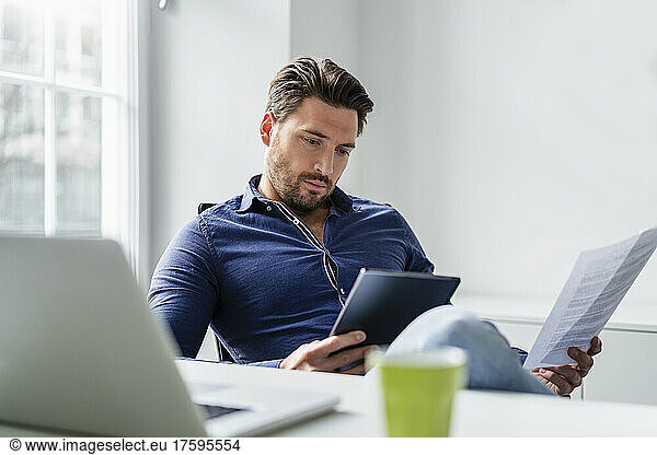 Businessman with document working on tablet PC in office
