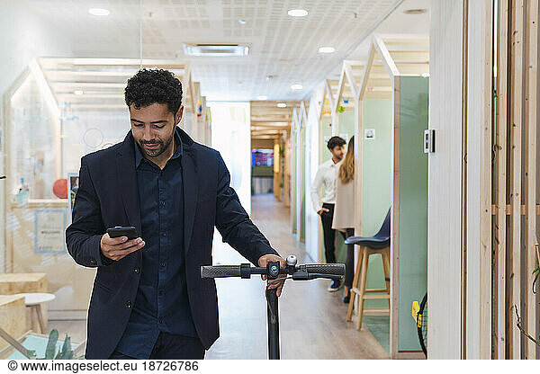 Businessman with electric scooter and mobile phone in office