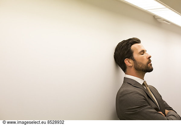 Businessman with eyes closed leaning against wall