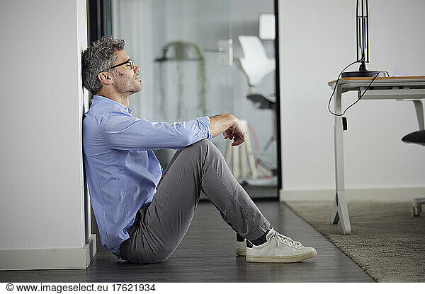 Businessman with eyes closed sitting by wall in office
