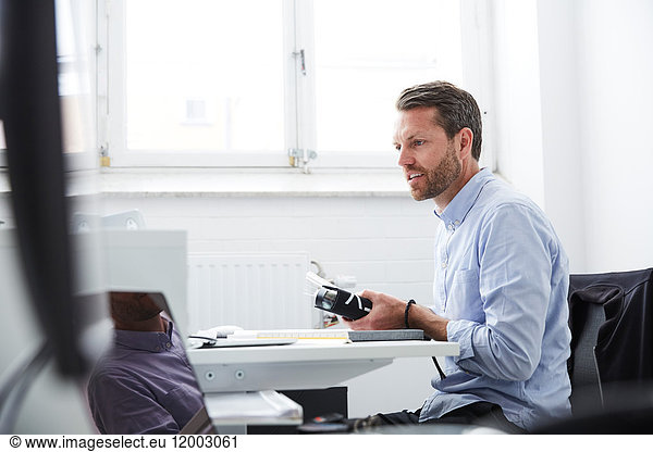 Businessman with folder looking at laptop while sitting in creative office