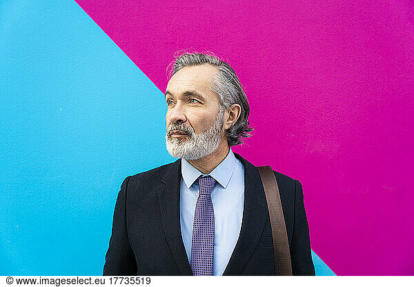 Businessman with gray hair standing in front of pink and blue wall