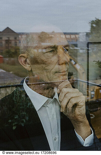 Businessman with hand on chin seen through glass at office