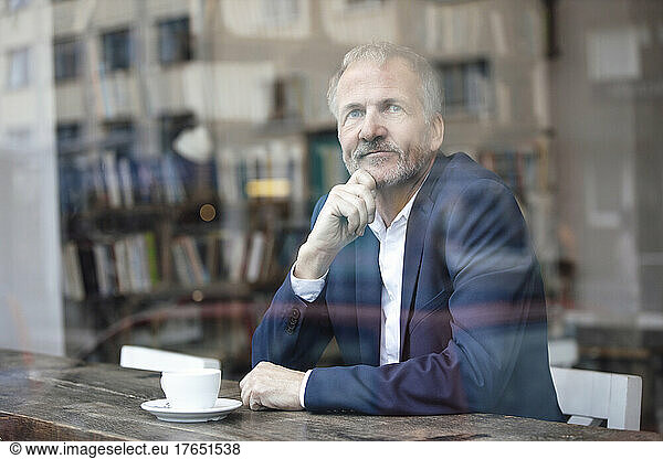 Businessman with hand on chin sitting at table by glass window