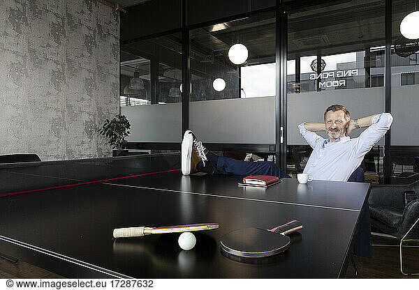 Businessman with hands behind head sitting at table tennis table in office