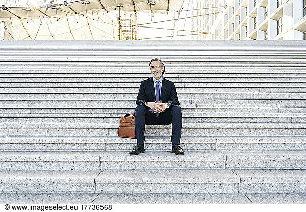 Businessman with hands clasped sitting on staircase