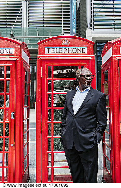 Businessman with hands in pockets standing near telephone booth