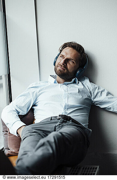 Businessman with headphones looking away while resting in office