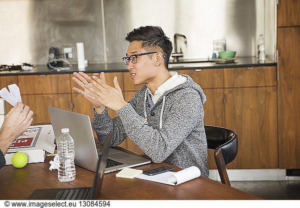 Businessman with laptop computer gesturing while sitting in creative office