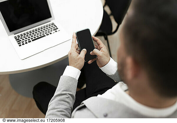 Businessman with laptop using smart phone in office