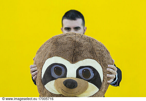 Businessman with meerkat mask in front of yellow wall