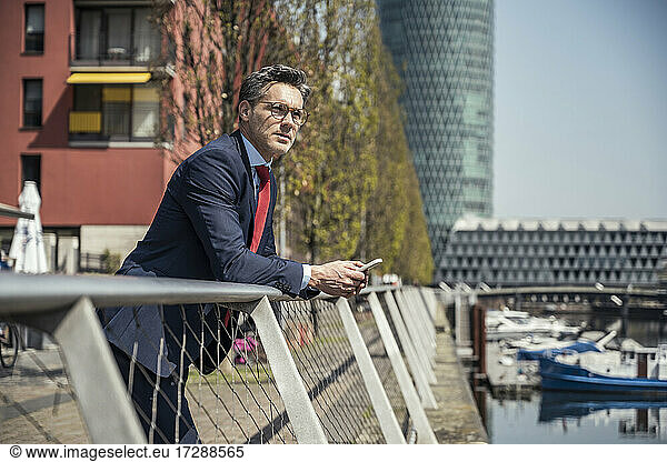 Businessman with mobile phone leaning on railing during sunny day