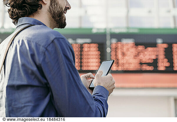 Businessman with mobile phone standing in front of arrival departure board